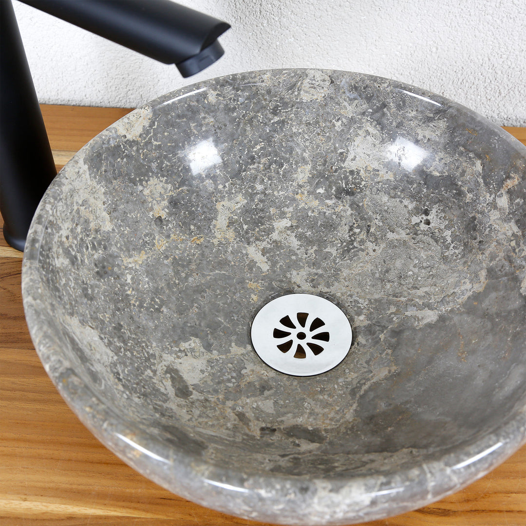 Vue du lavabo à poser en pierre naturelle avec grain gris-brun et couvercle d'écoulement en acier inoxydable, associé à un robinet sur pied noir