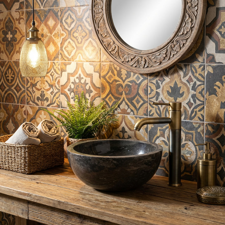 Ronde opzetwastafel van steen op een houten wastafel met messing beslag voor patroontegels in een warme badkamersfeer