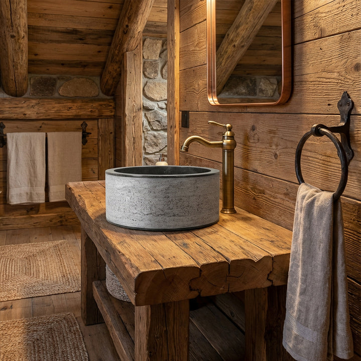 Ronde opzetwastafel van steen op een massief houten tafel, gecombineerd met messing beslag in een rustieke chaletbadkamer.
