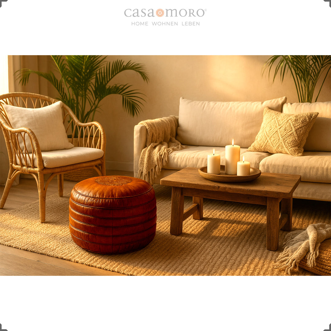 Scène de salon chaleureuse avec un pouf rond en cuir véritable marron devant un canapé et une table en bois avec des bougies - ambiance bohème chaleureuse dans la lumière du soir.