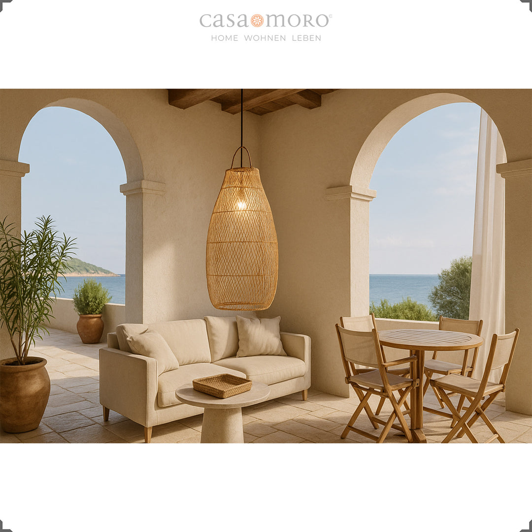 Hohe Rattanlampe auf mediterraner Terrasse über Esstisch und Sofa mit Blick aufs Meer