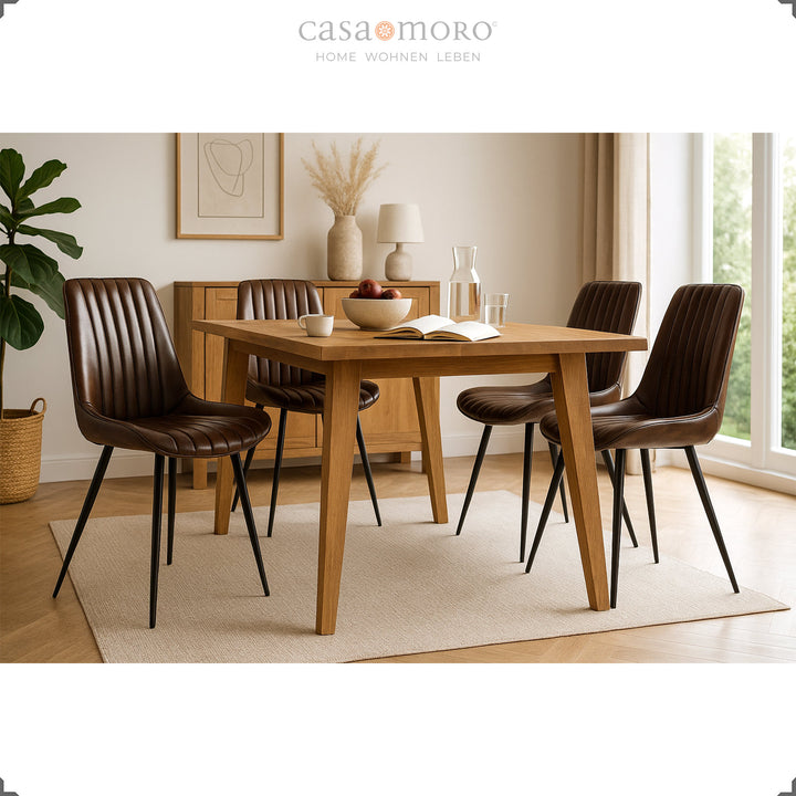 Vier antieke bruinleren stoelen met zwart gelakte metalen poten aan een rechthoekige houten tafel in een lichte keuken met natuurlijk licht