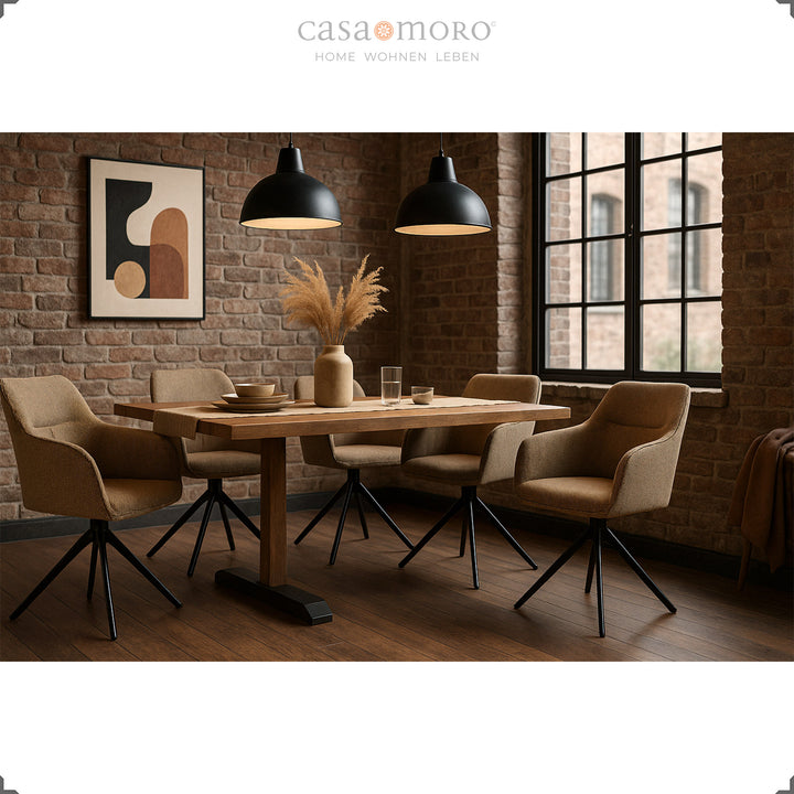 Quatre chaises rembourrées pivotantes à 360° avec accoudoirs marron sur une table en bois dans une salle à manger moderne avec un mur de briques, des lampes noires et une lumière chaude