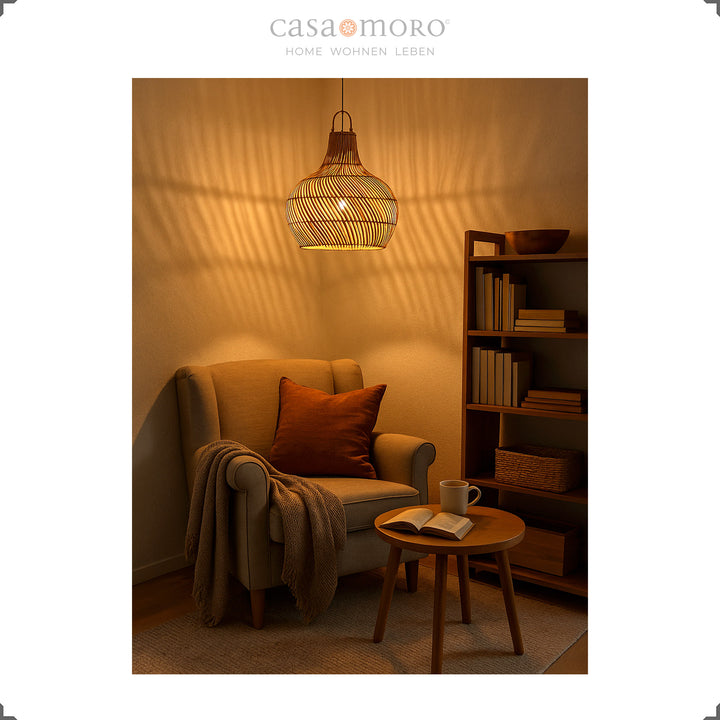 Une lampe en rotin suspendue avec une lumière chaude au-dessus d'une chaise de lecture crée un jeu d'ombres atmosphérique sur le mur