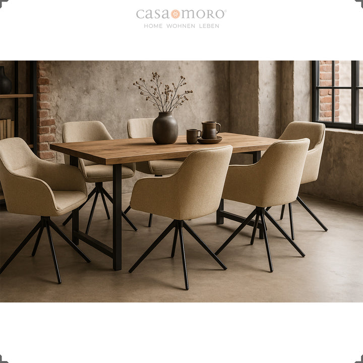 Six chaises rembourrées pivotantes à 360° avec accoudoirs beiges autour d'une table en bois dans une salle à manger moderne avec murs en béton et structure en métal noir