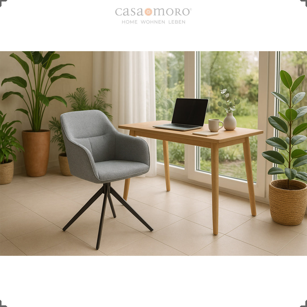 Chaise rembourrée rotative à 360° avec accoudoirs gris sur une table en bois avec un ordinateur portable, encadrée de plantes et de grandes fenêtres dans un environnement de vie lumineux