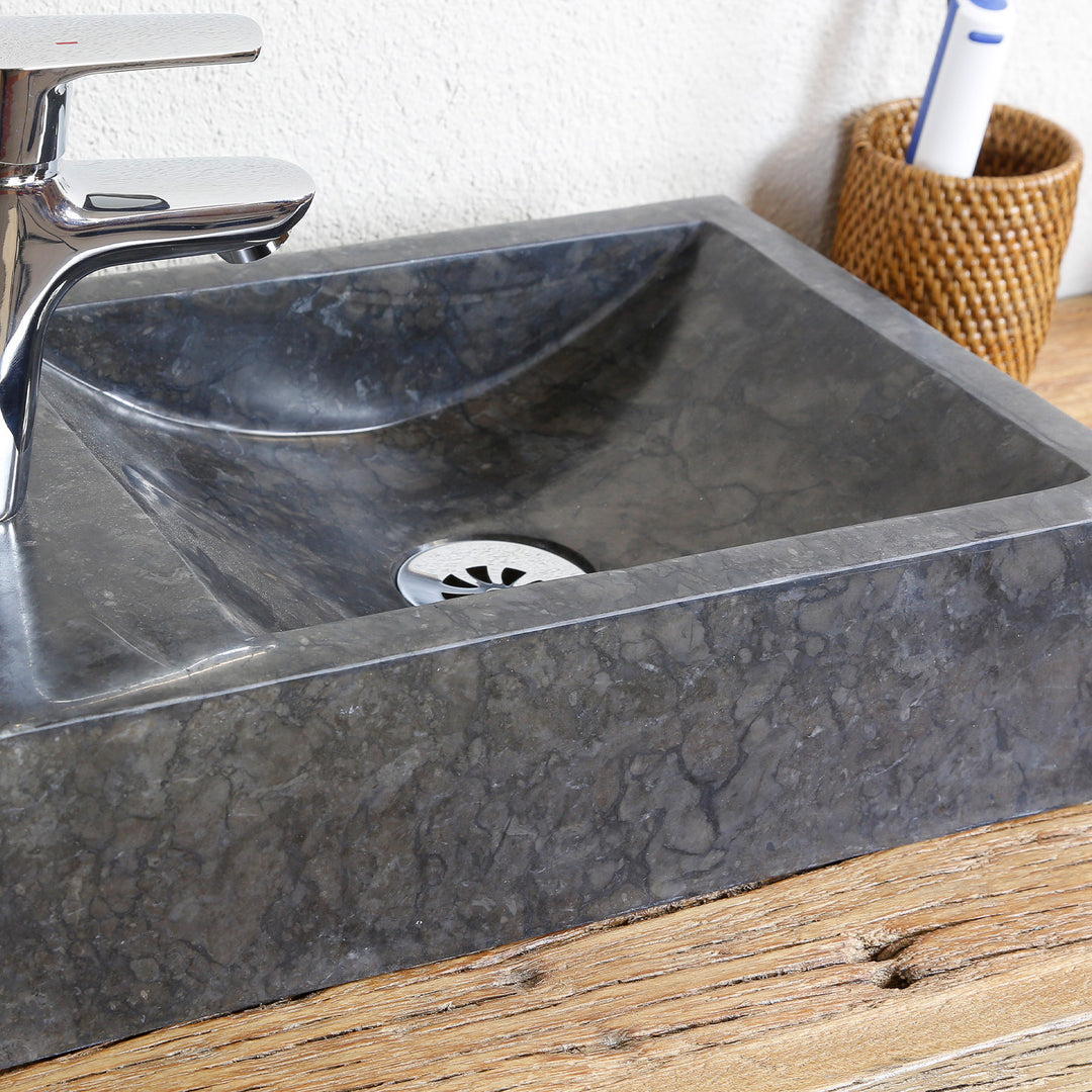 Hoekige natuurstenen opzetwastafel met donkere nerf in gedetailleerd aanzicht, met RVS afvoer en verchroomd beslag op houten plaat