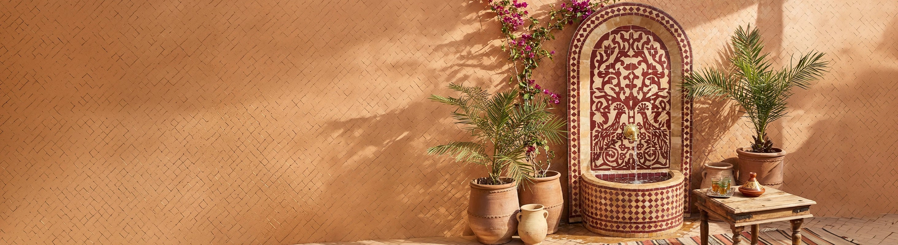 fontaine en mosaïque – Marokkanischer Mosaikbrunnen mit Zellige-Fliesen als Wasserbrunnen im Garten vor warmer Wand mit Pflanzen und orientalischer Atmosphäre