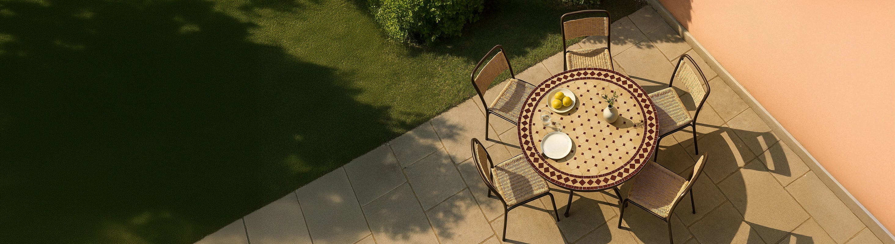 Mozaïektafels Ø100 – Grote ronde mozaïektafel Ø100 cm met zellige tegels en diverse stoelen op het terras in de tuin vanuit vogelperspectief met warme zon