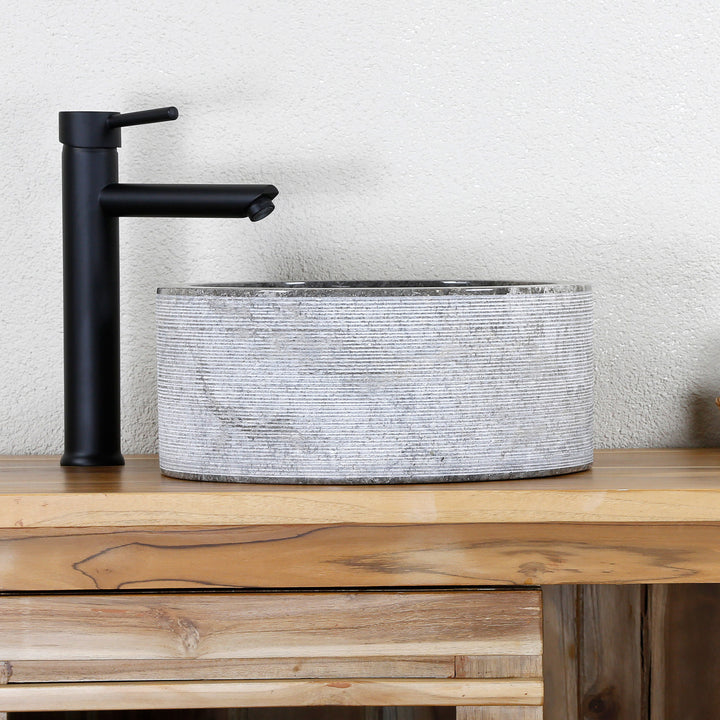 Moderne Lavabo Fabriqué en pierre naturelle claire avec une structure aux lignes fines et des ferrures noires sur une console en bois.