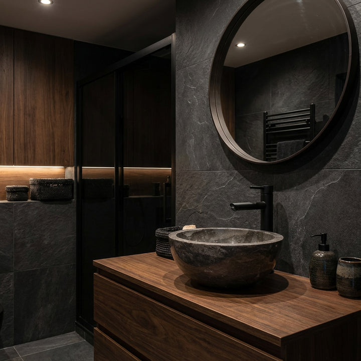 Ronde natuursteenWastafel als opzetstuk op een donkerhouten wastafel met zwart armatuur in een elegante, donkere badkamersfeer