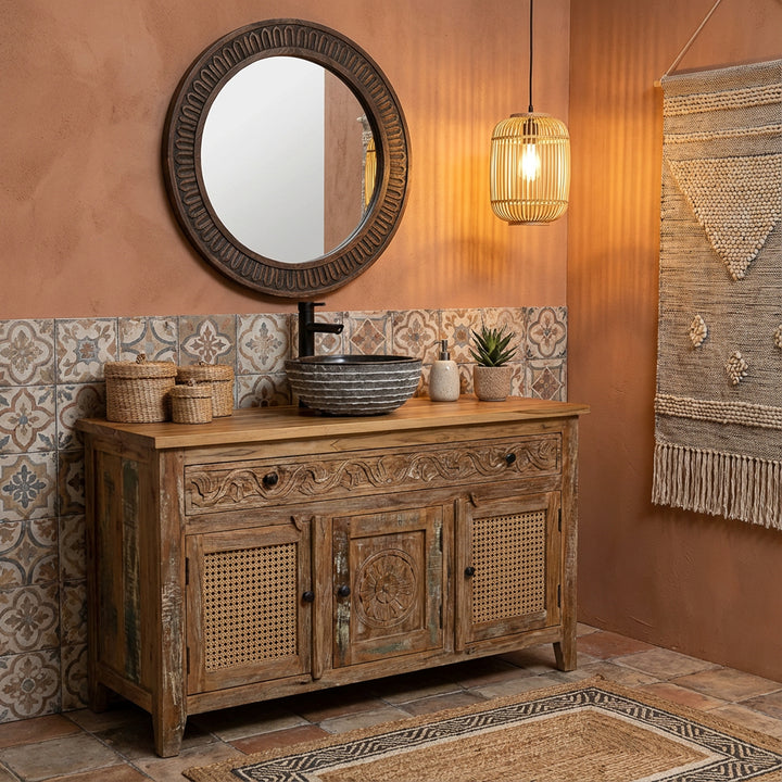Lavabo rond en pierre sur meuble-lavabo en bois sculpté dans une salle de bains bohème chaleureuse avec carrelage, miroir et suspension