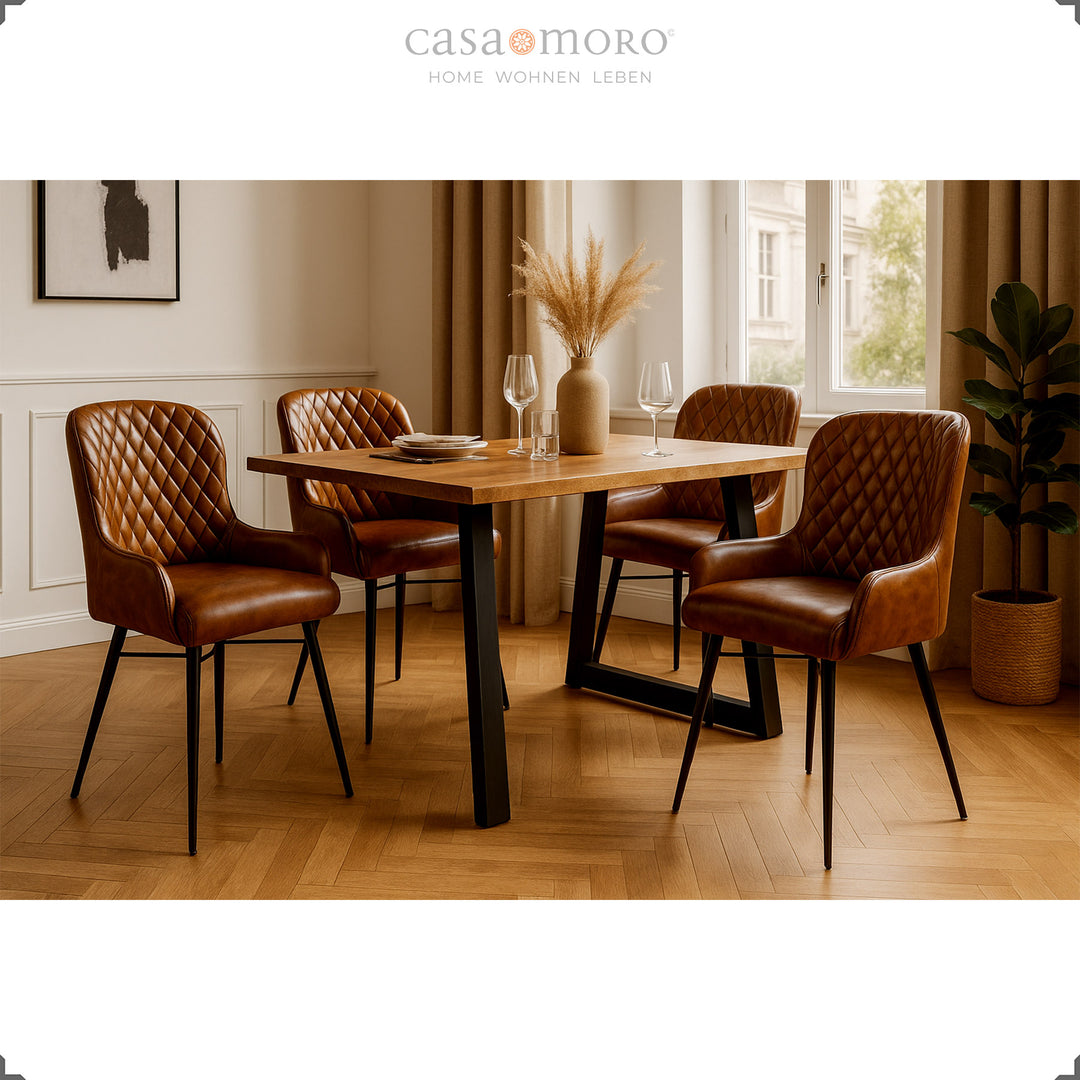 Vier antieke bruinleren stoelen met diamantquilt aan een houten tafel in een elegante eetkamer met parketvloer, lichte lambrisering en natuurlijke decoraties.