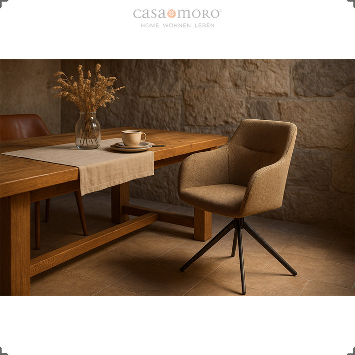 Chaise rembourrée rotative à 360° avec accoudoirs marron sur une table en bois dans une salle à manger avec un mur en pierre naturelle et une ambiance lumineuse chaleureuse