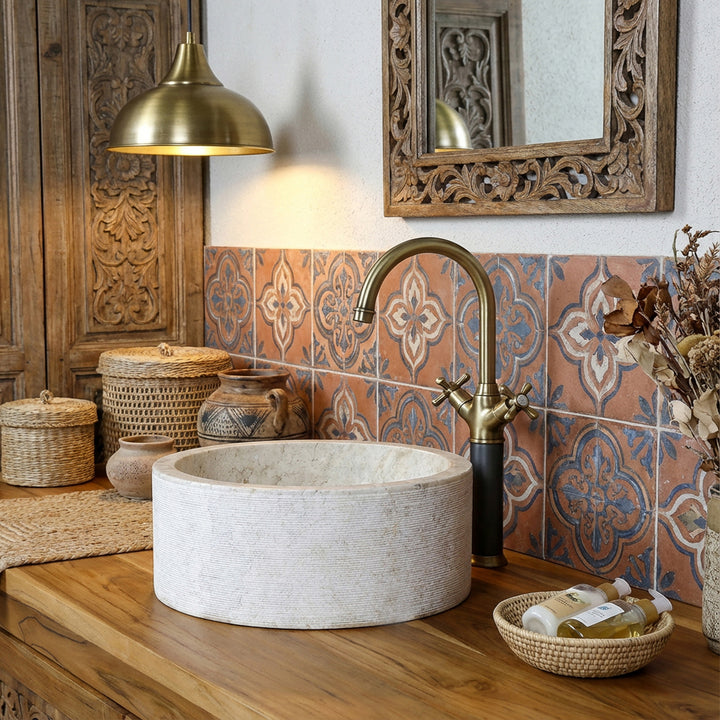 Lavabo rond en pierre au look marbre chaleureux sur une console en bois, complété par des robinetteries en laiton et des carreaux orientaux.
