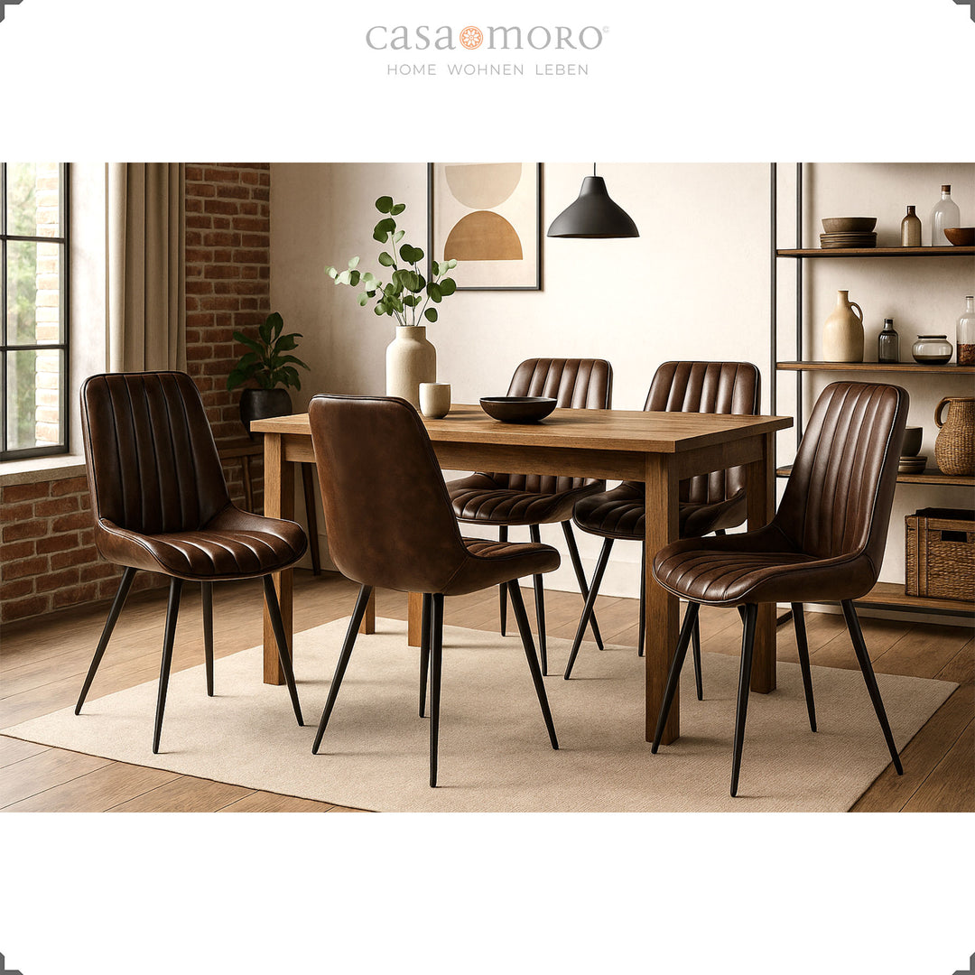 Antieke bruin lederen stoelen met zwart geschilderde metalen poten rond een rechthoekige houten tafel in moderne eetkamer met bakstenen muur