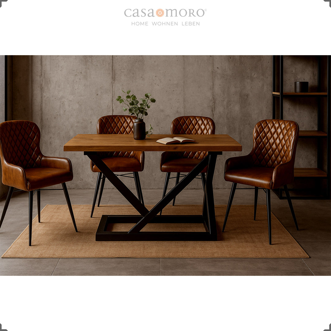 Vier antieke bruinleren stoelen met diamantquilt aan een moderne houten tafel met een zwart metalen frame in een elegante loft-eetkamer met een betonnen muur.