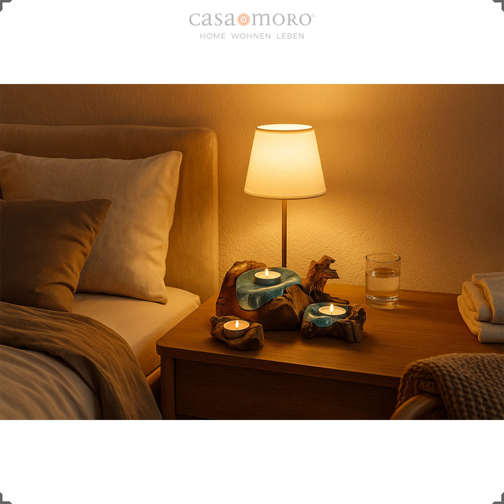 Drie theelichthouders van glas en wortelhout op een nachtkastje, waarvan het zachte kaarslicht een rustgevende slaapkamersfeer creëert.