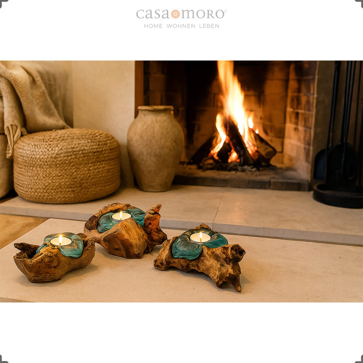 Drie theelichthouders van glas en wortelhout voor een brandende open haard, hun zachte licht onderstreept de gezellige woonsfeer.