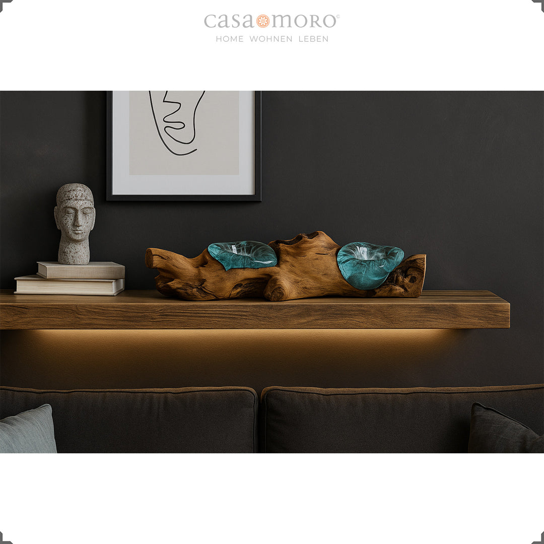 Langwerpige theelichthouder van glas en wortelhout op een wandplank, het warme licht complementeert de stijlvol donkere woonkamersfeer.