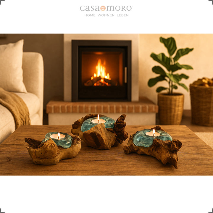 Drie theelichthouders van glas en wortelhout op een houten tafel, hun warme licht complementeert de gezellige open haardsfeer in de woonkamer.