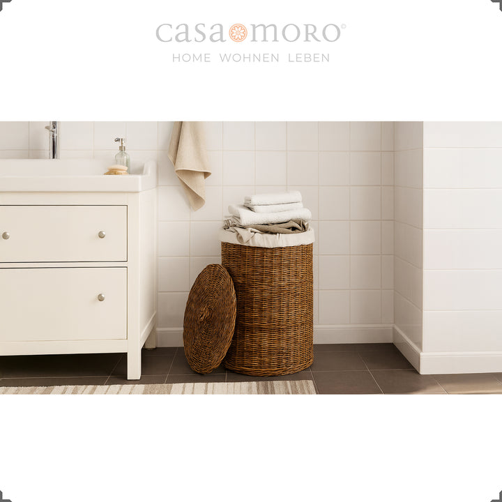 Panier à linge en rotin marron foncé avec couvercle et sac intérieur dans une salle de bain claire, décoré de serviettes