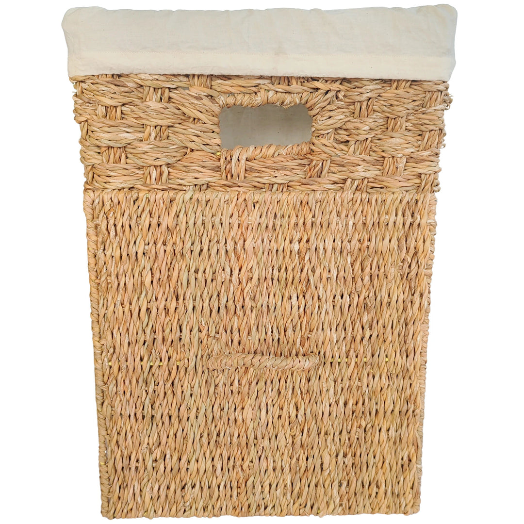 Panier à linge carré en jonc de mer, bord de sac clair et couvercle rectangulaire tressé appuyé devant.