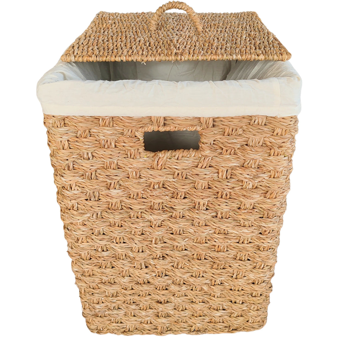 Panier à linge carré en jonc de mer, couvercle soulevé en biais et sac clair derrière l’ouverture de prise.