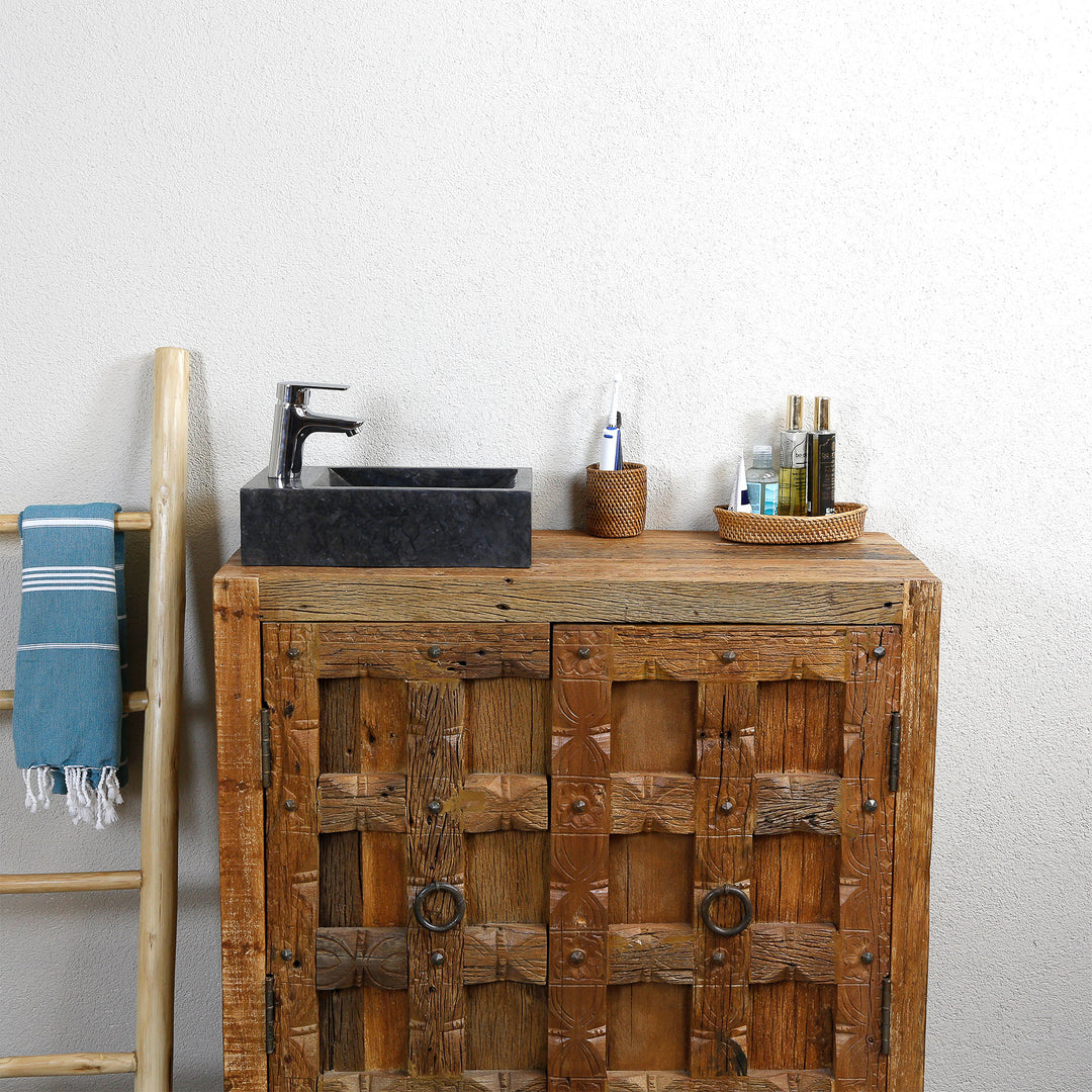 Vierkante opzetwastafel van marmer met donkere nerf op een rustieke houten wastafel, gecombineerd met verchroomd beslag en natuurlijke accessoires voor een lichte wand