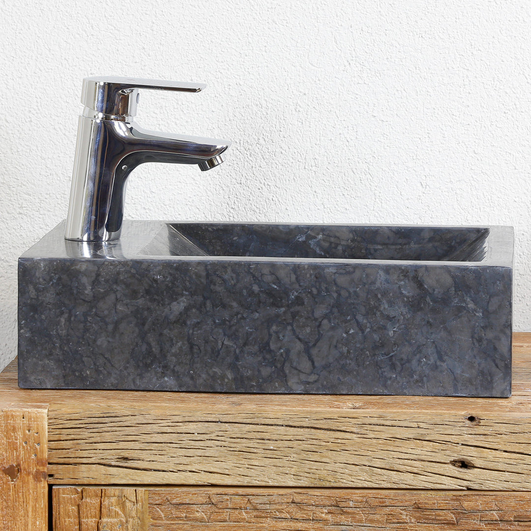 Vierkante opzetwastafel van marmer met donkere nerf op een houten console, gecombineerd met verchroomd beslag voor een lichte wand