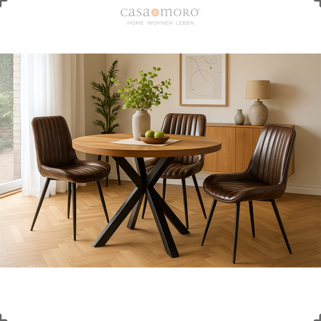 Drie antieke bruinleren stoelen met zwart gelakte metalen poten aan een ronde houten tafel in de lichte woonkamer met parketvloer